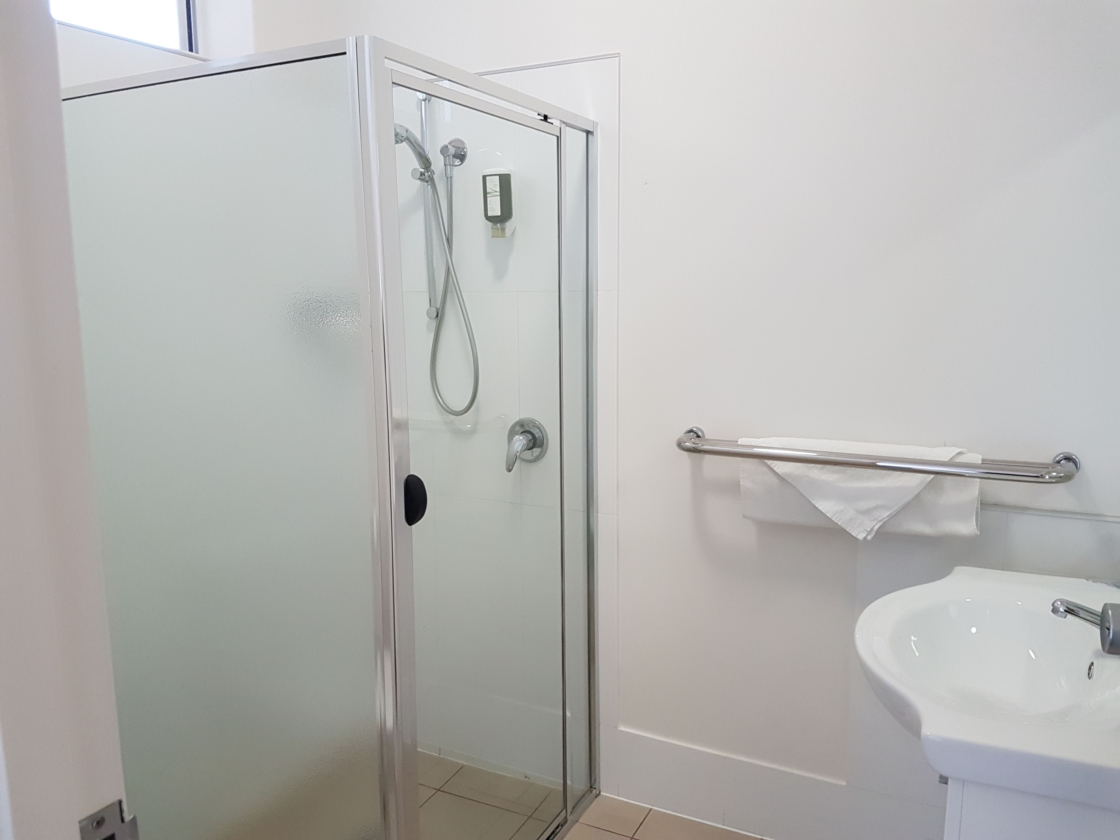 A bathroom with a glass-enclosed shower, a white sink, and a towel rack.