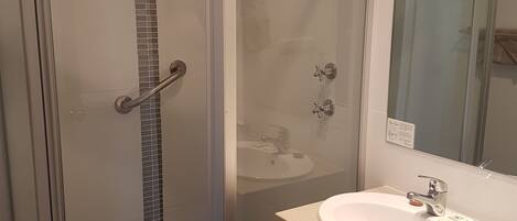 Un baño moderno con ducha envuelta en cristal, lavamanos con espejo y perchero para toallas.