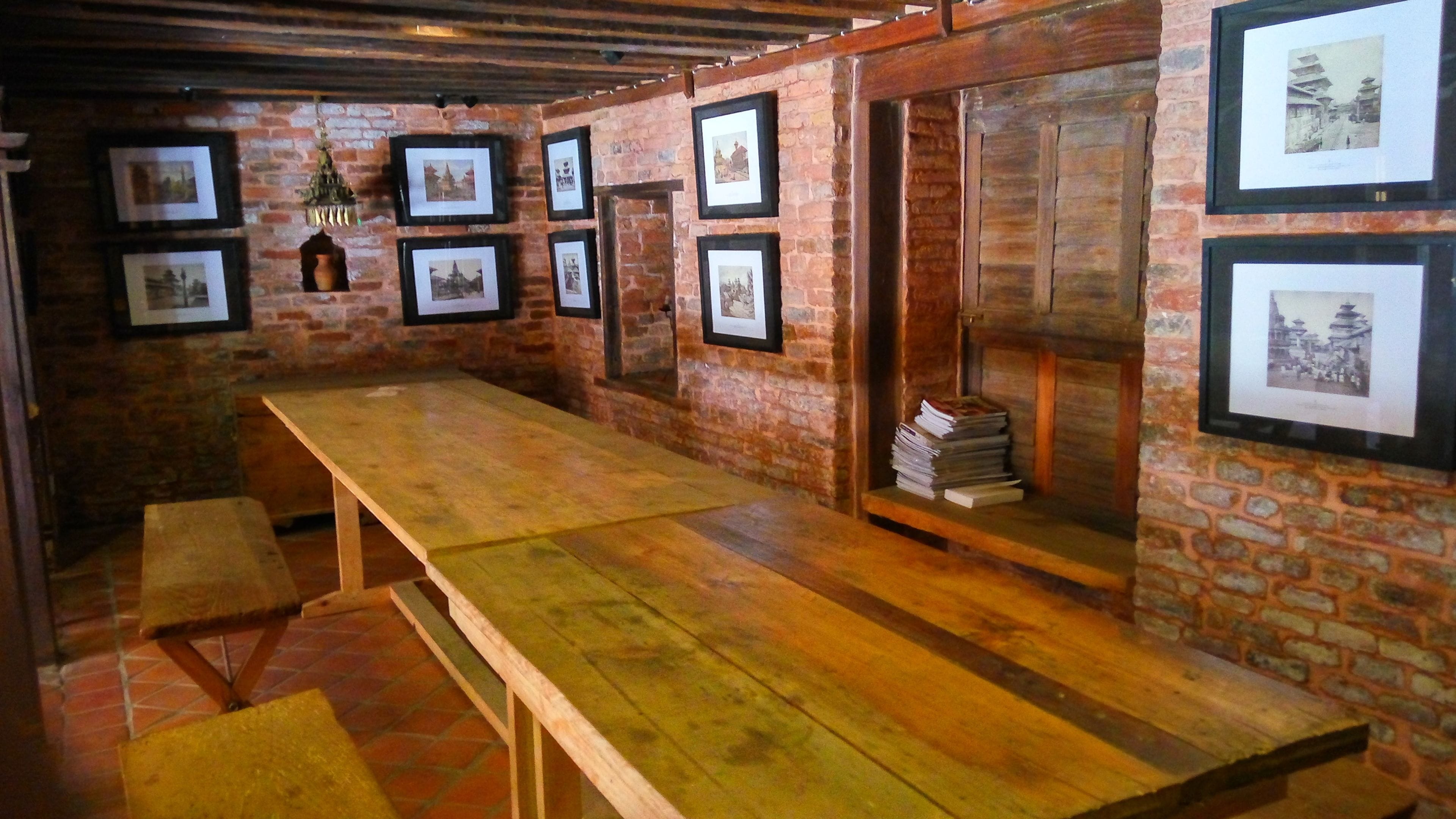 Una habitación rústica con una larga mesa de madera, bancos y paredes de ladrillo decoradas con cuadros.