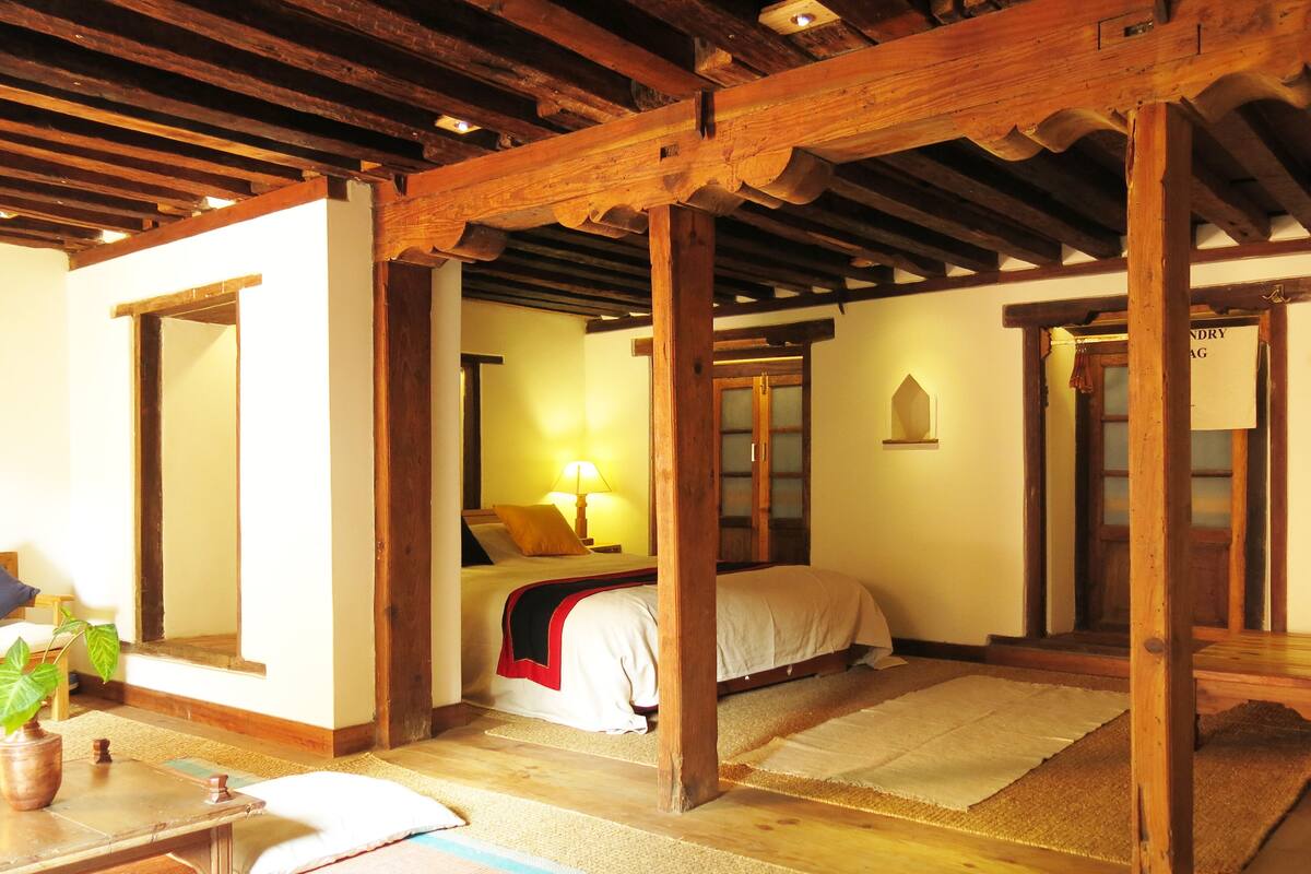 A traditional room with wooden beams, a bed with a red blanket, a lamp, and a mirror.
