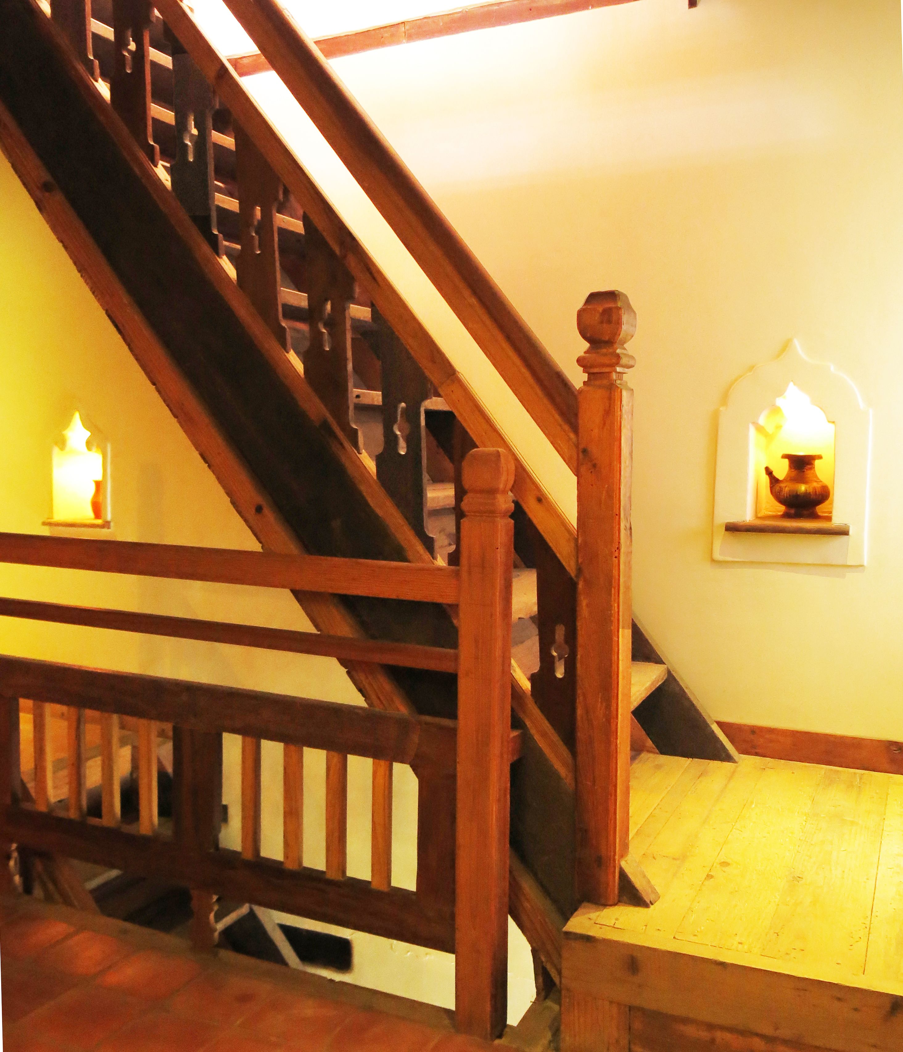 A wooden staircase with a handrail and a small table at the bottom. There are two wall-mounted sconces with candles.