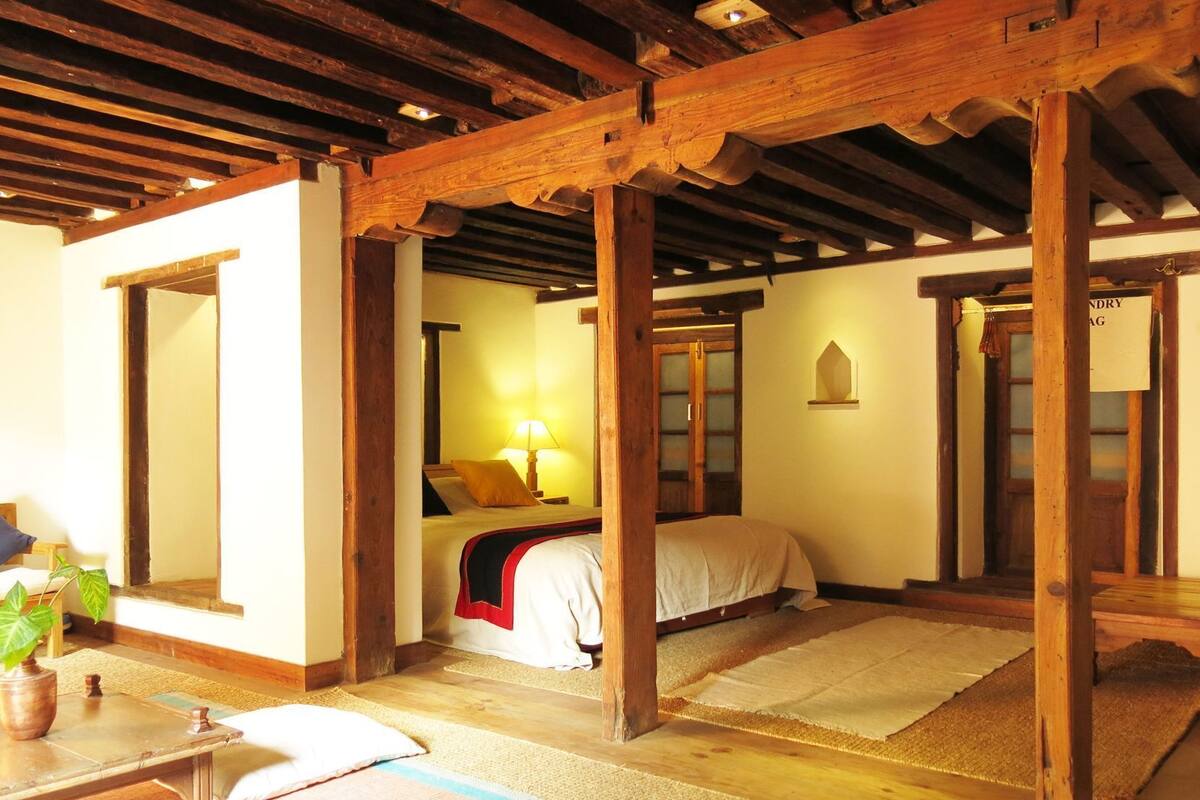 A traditional room with a bed, a nightstand, a lamp, and a wooden ceiling structure.
