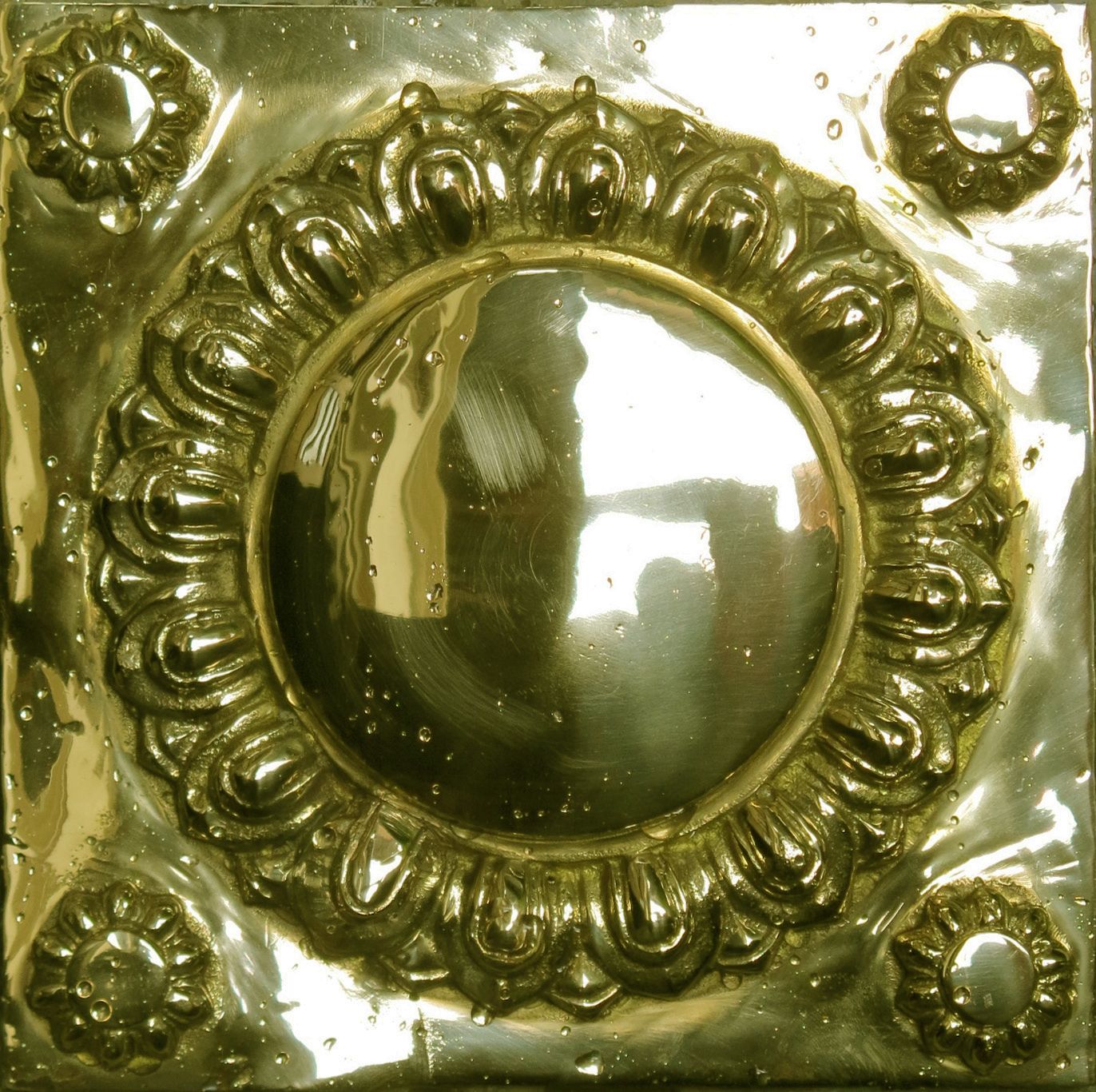 Un objet métallique doté d’une surface circulaire centrale réfléchissante, entourée de motifs décoratifs en relief.