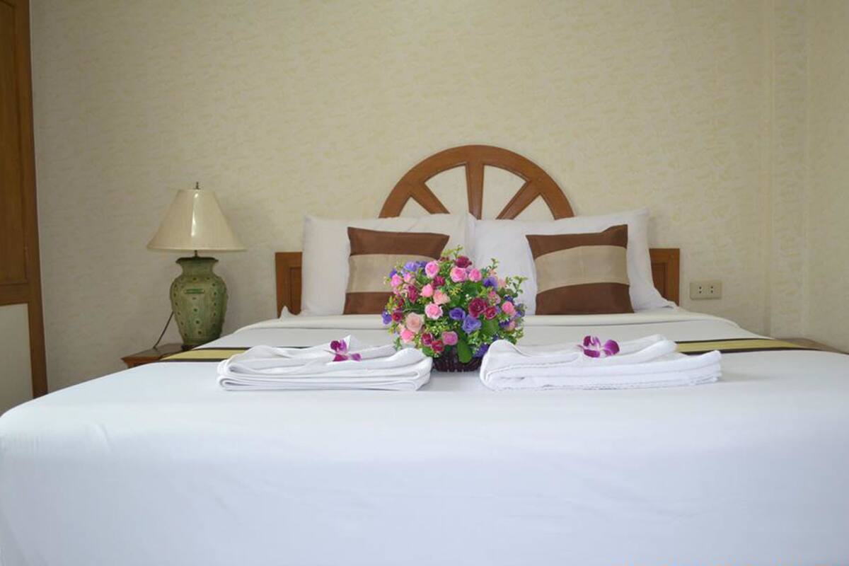 A neatly made bed with white linens, a floral centerpiece, and folded towels.