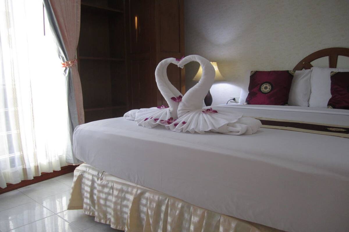 A hotel room with a neatly made bed, a large window with curtains, and a wooden headboard.