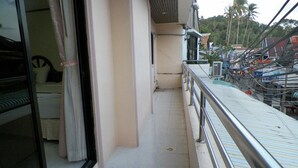 A narrow balcony with a metal railing, a tiled floor, and a view of a residential area with houses and palm trees. - Natacha Hotel (Ko Phi Phi)