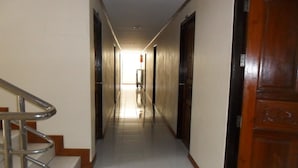 A hallway with a wooden door on the right, a metal railing on the left, and a tiled floor. - Natacha Hotel (Ko Phi Phi)