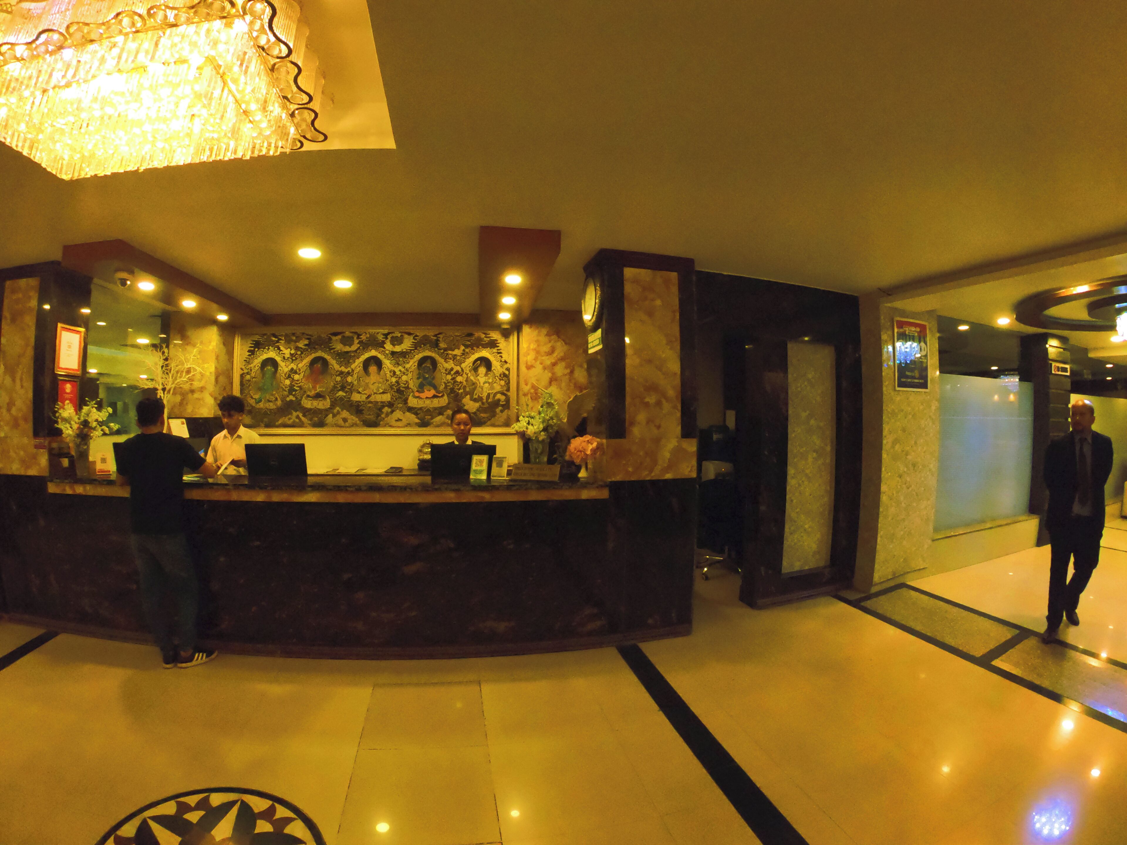 A hotel reception area with a marble counter, a large decorative wall, and a modern chandelier.
