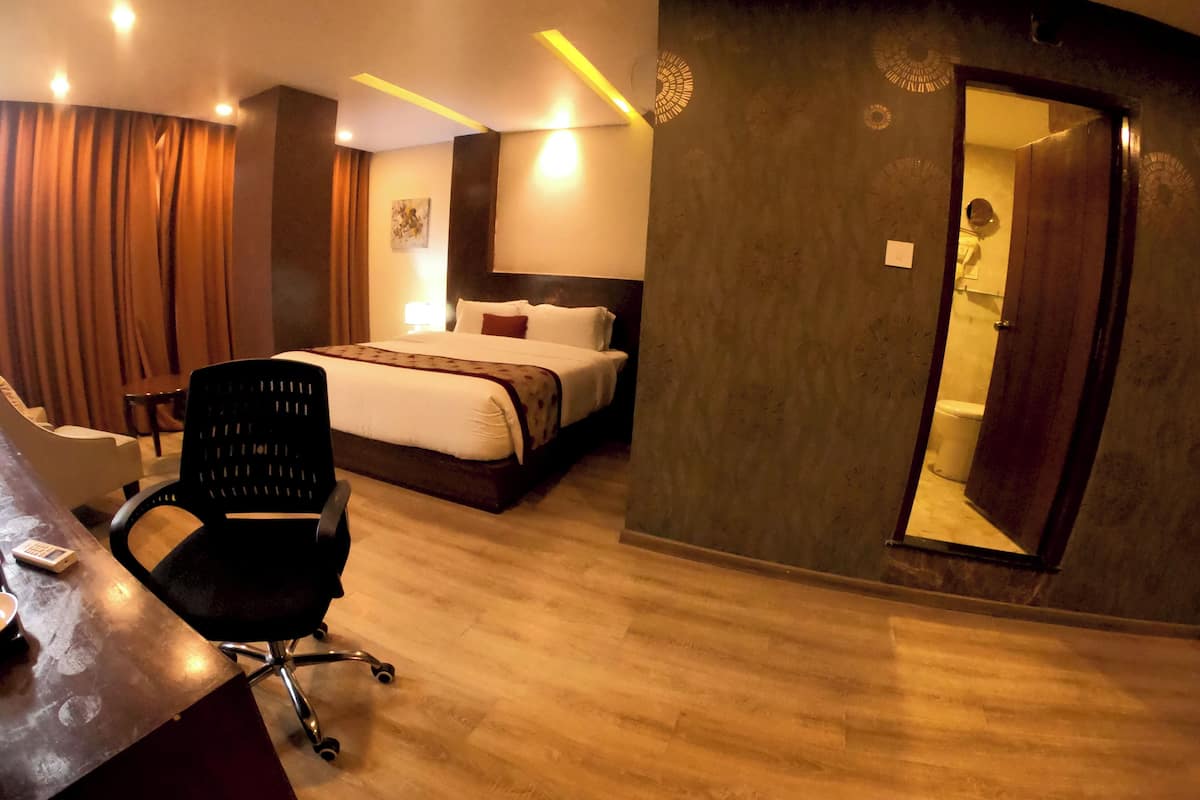 A hotel room with a bed, a desk with a chair, a bathroom visible through an open door, and a wooden floor.