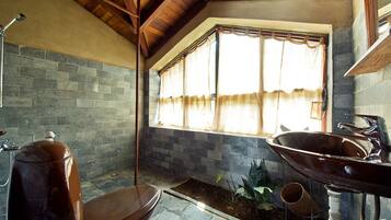 A bathroom with a stone wall, a large window with curtains, a wooden bench, and a sink.