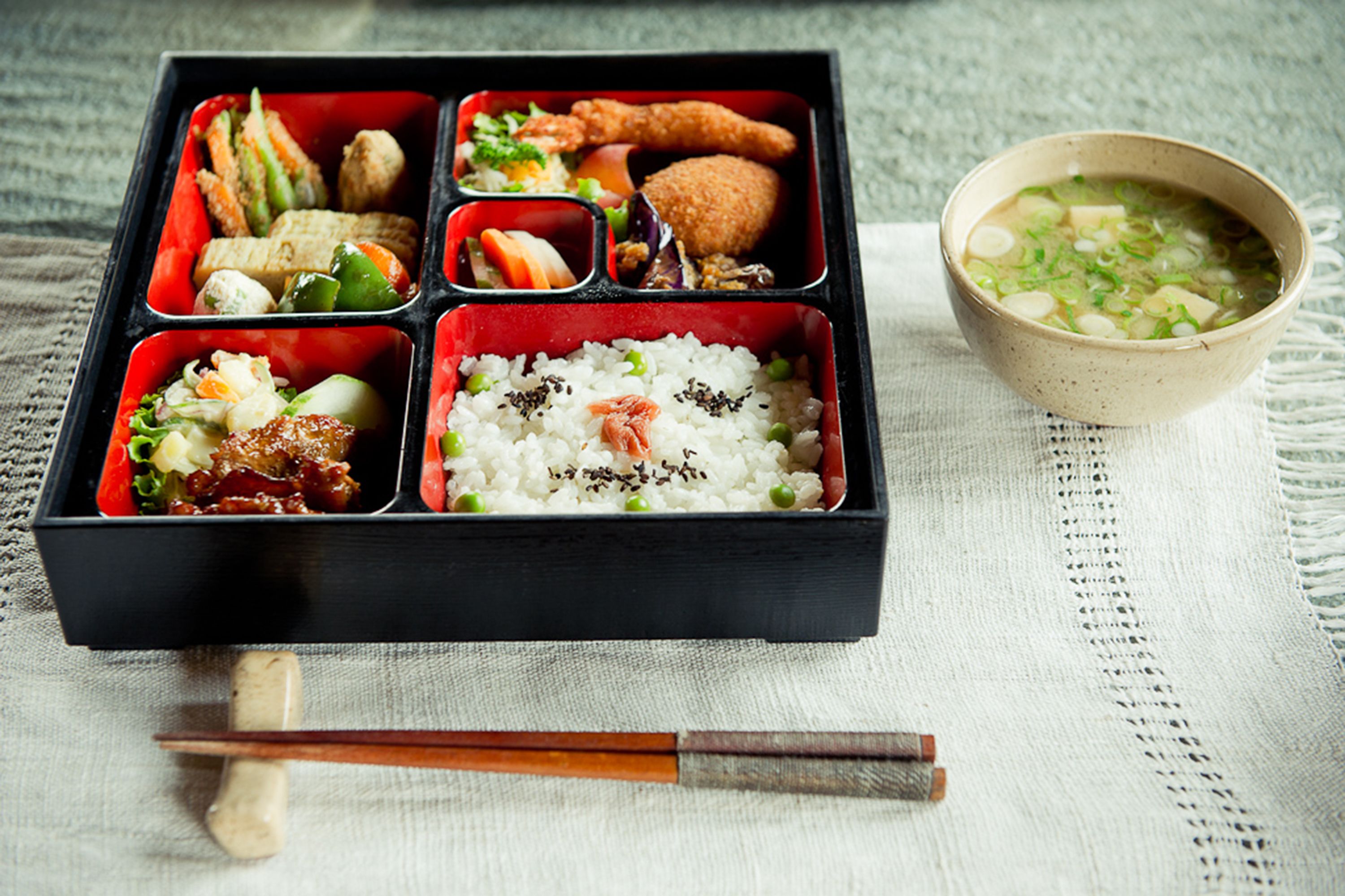 A bento box with various food items and a bowl of soup.