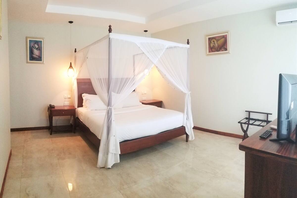 Quarto bem arrumado com cama de dossel, abajures, escrivaninha com computador e obras de arte nas paredes.