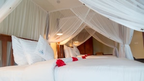 A bed with white bedding and red flowers, a wooden headboard, and sheer white curtains.