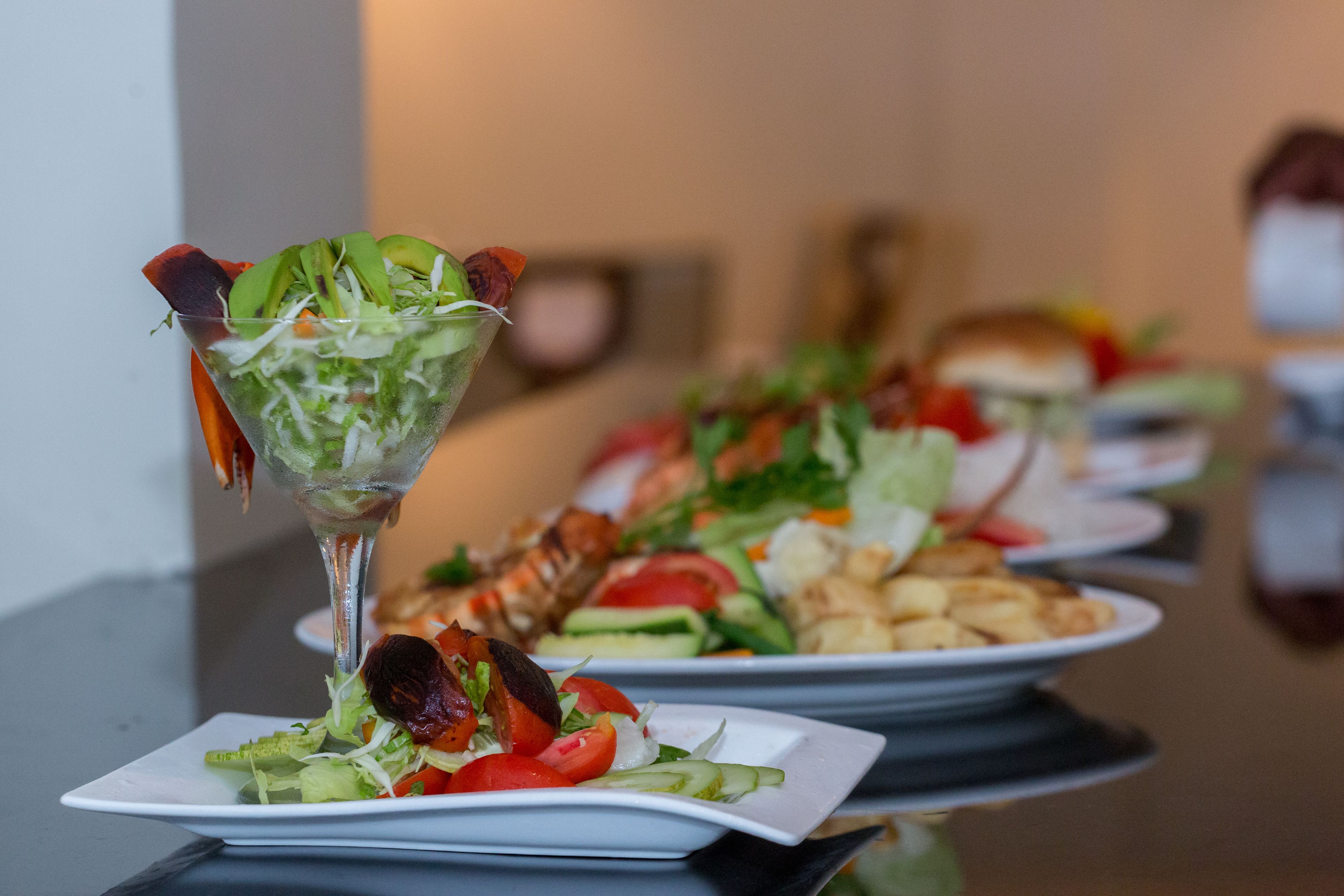 Une table à manger avec différents plats, notamment une salade servie dans un verre, des assiettes de légumes et une queue de homard.