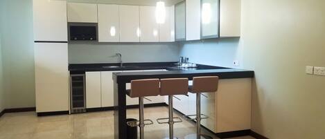 A modern kitchen with white cabinets, a black countertop, and a built-in microwave. There are three bar stools with metal frames and cushioned seats.