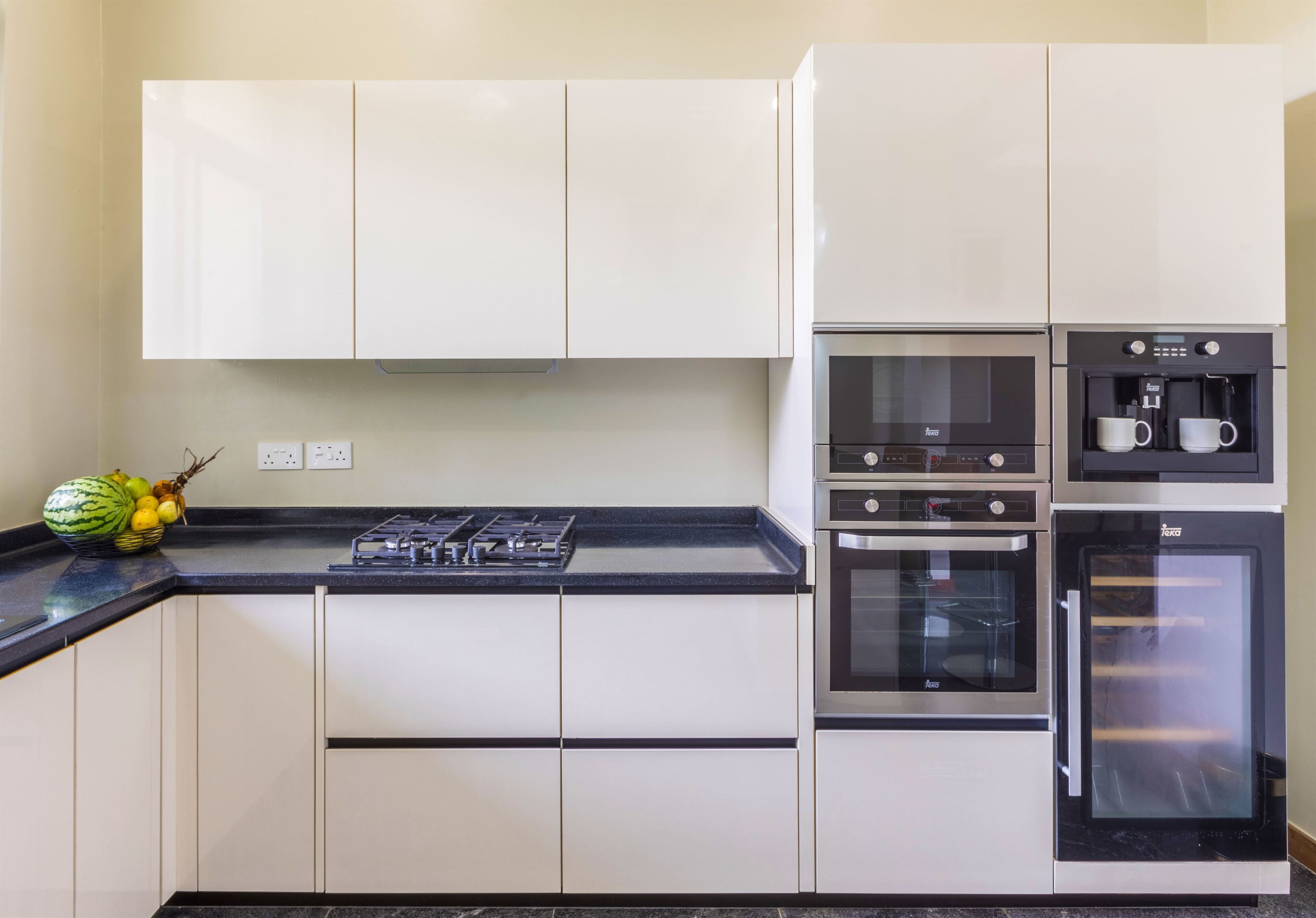 Una cocina moderna con armarios blancos, encimera negra, estufa integrada, horno y cafetera.