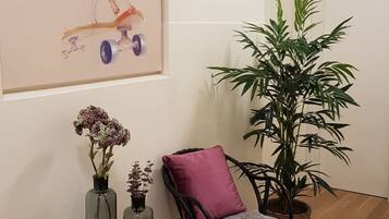 Una habitación con una obra de arte enmarcada de un perro, una silla con un cojín morado, una planta en maceta y una mesita con jarrones.