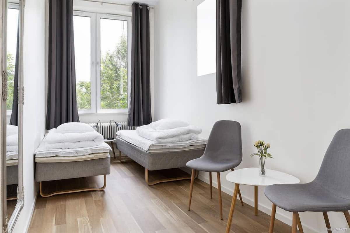 A modern hotel room with two single beds, a small table, two chairs, and a window with curtains.