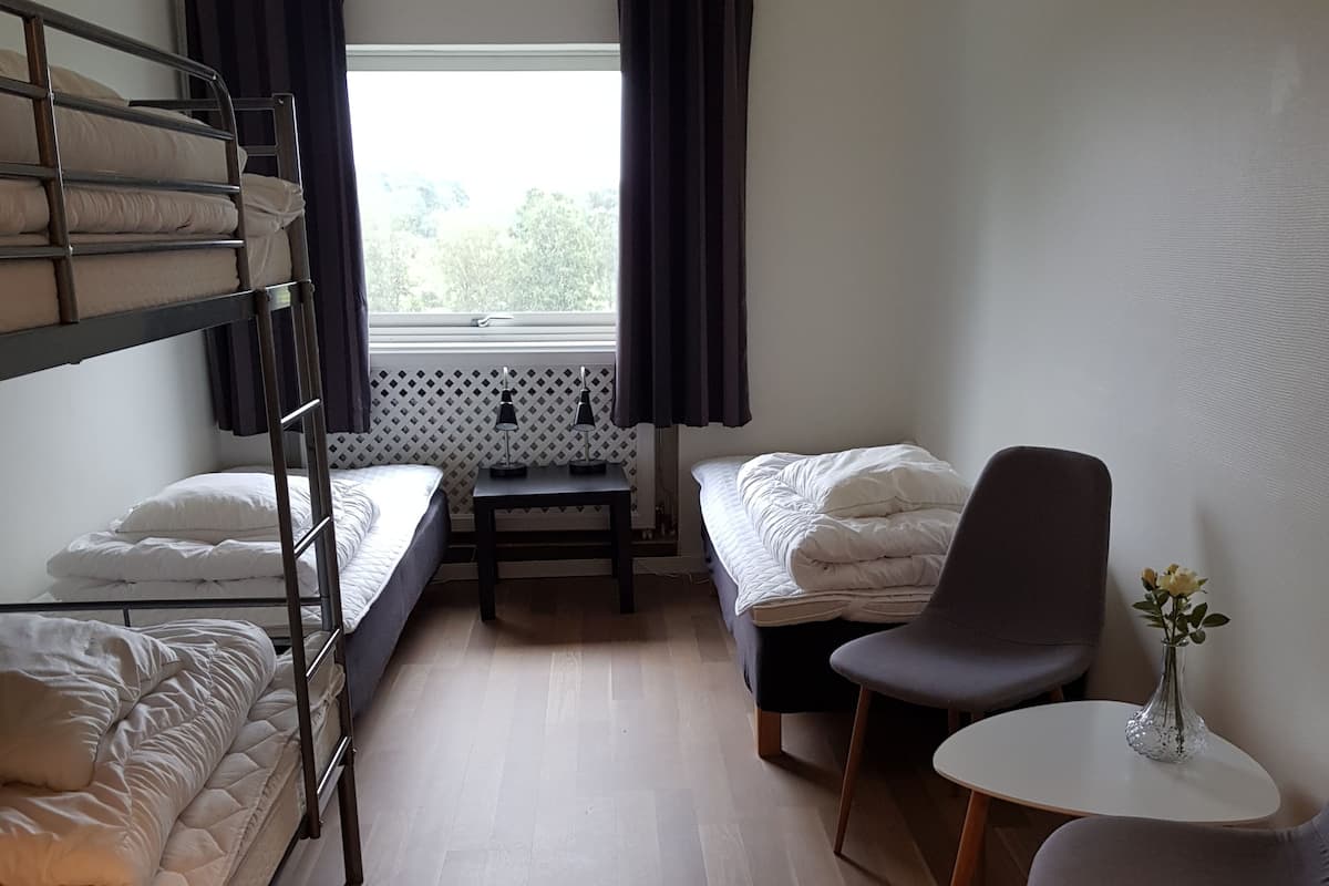A compact room with bunk beds, a small table with two lamps, a chair, and a vase with flowers.
