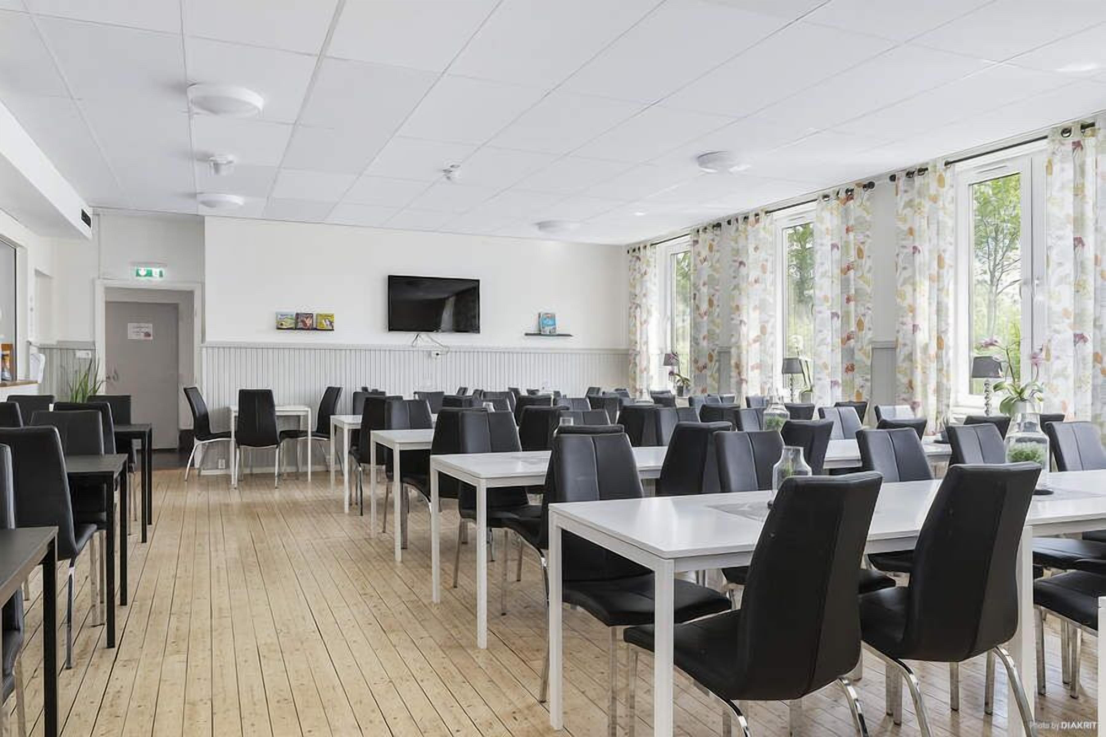 Une salle de conférence équipée de tables et de chaises, d’un téléviseur fixé au mur et de grandes fenêtres avec des rideaux.