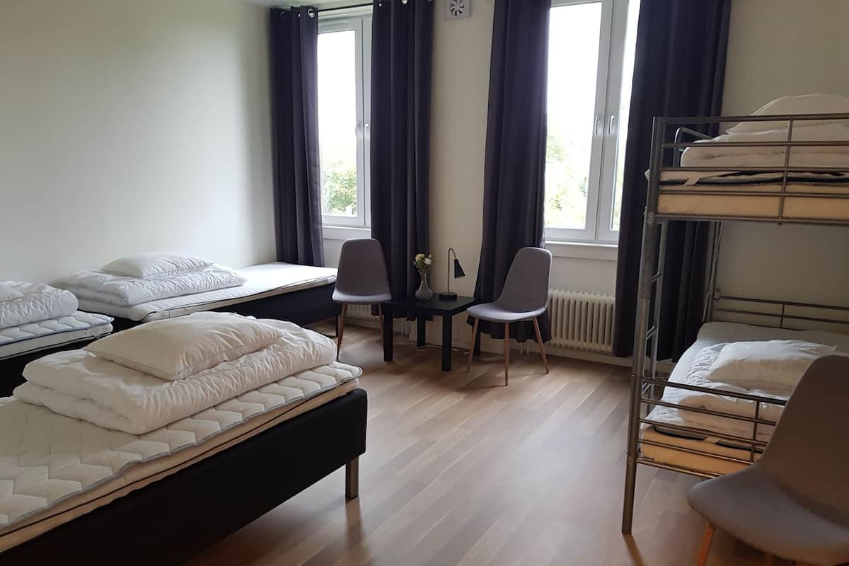 A dormitory room with bunk beds, a desk, two chairs, and a radiator.
