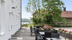 An outdoor patio with tables and chairs, a wooden fence, and a building with a red roof.