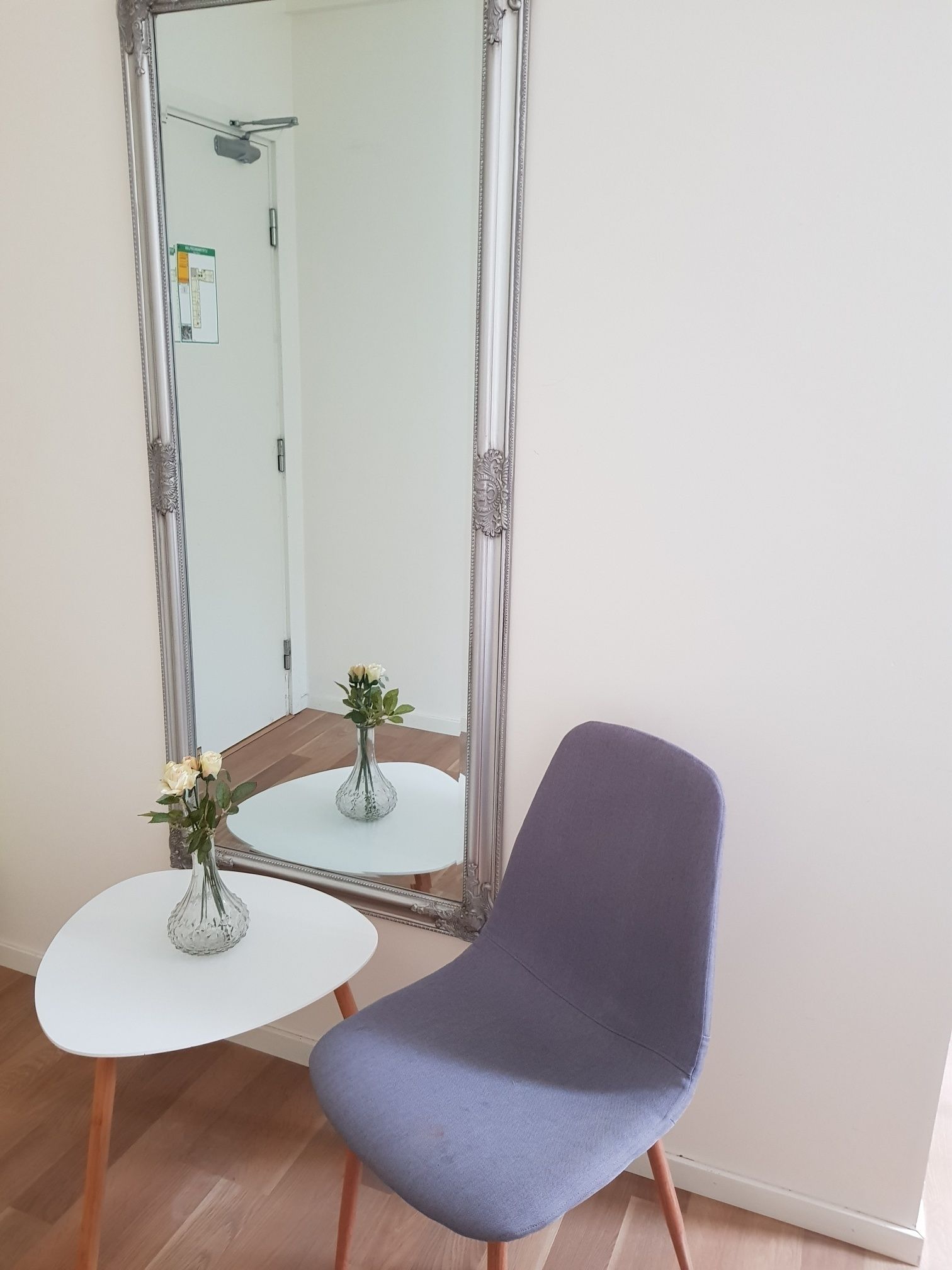 A room with a large ornate mirror, a small white table with a vase of flowers, and a purple chair.