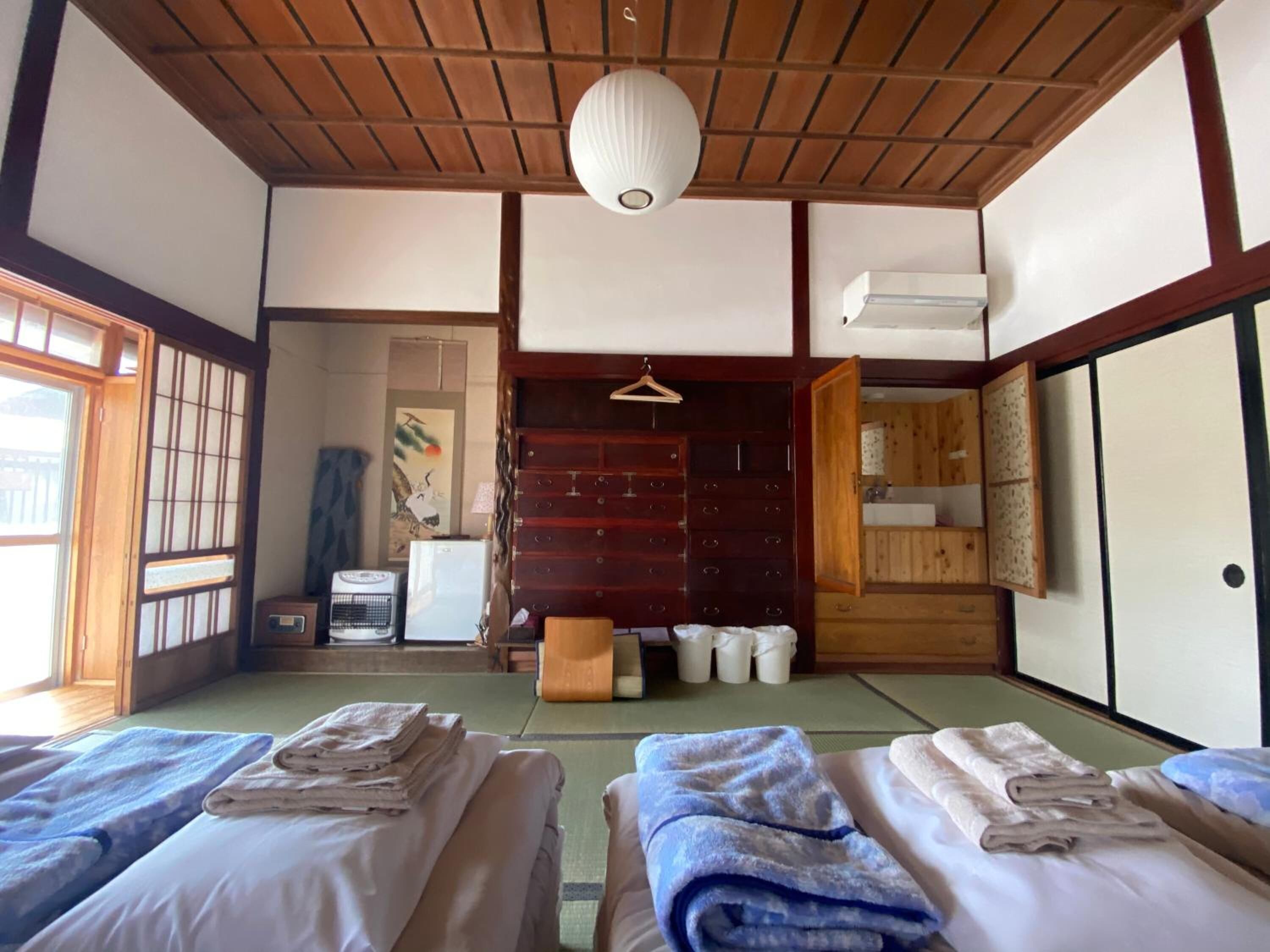 A traditional Japanese room with tatami flooring, two beds with towels, a wooden wardrobe, and a hanging lantern.