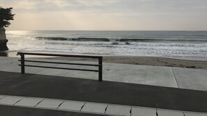 Un banco con vista a una playa, olas y un acantilado rocoso.