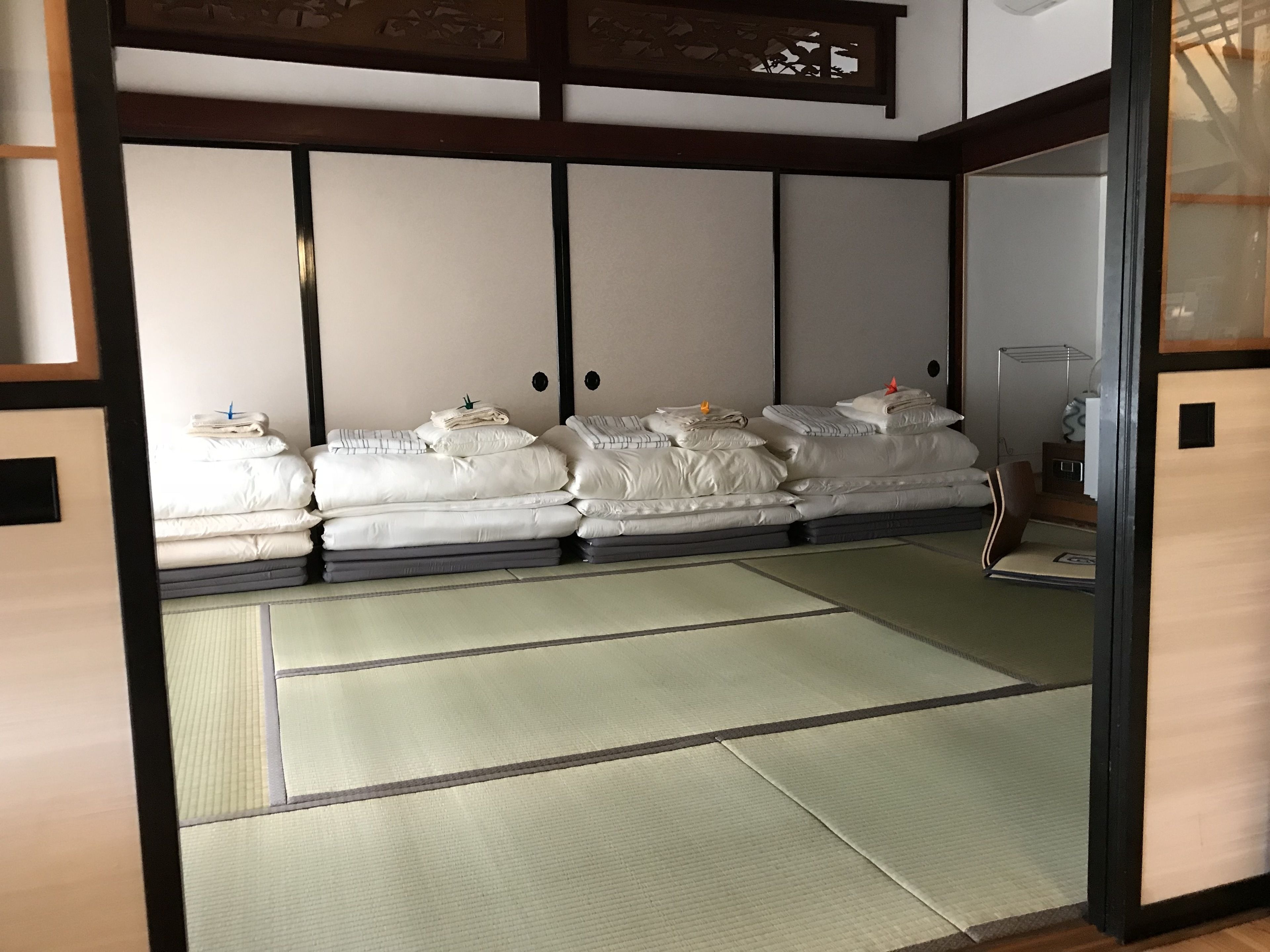 Une pièce de style japonais traditionnel, avec un sol recouvert de tatamis, un lit bas en bois avec une literie blanche et une porte coulissante en papier de riz (shoji).