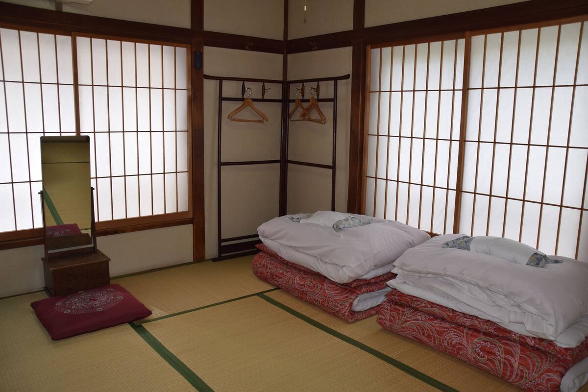 A traditional Japanese room with tatami flooring, a bed with white bedding, a wooden wardrobe, and a sliding door with a mirror.