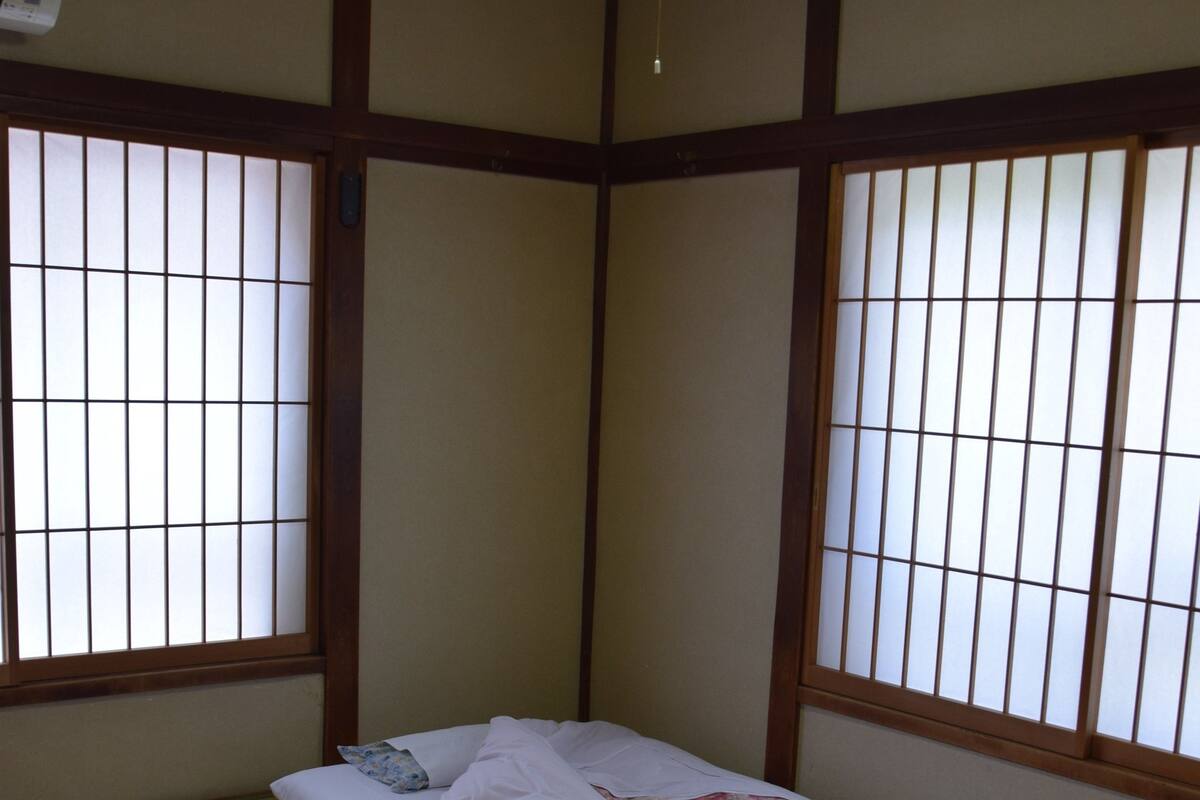 A traditional Japanese room with tatami flooring, a futon bed, a low wooden table with a bowl and chopsticks, and shoji screens.