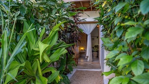 Un sentiero conduce a una stanza con una tenda bianca e un letto, immersa nel verde.