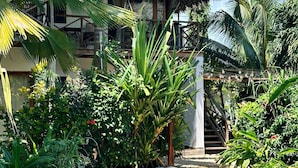 Un'area piscina con acqua cristallina, circondata da vegetazione rigogliosa e un edificio con tetto di paglia.