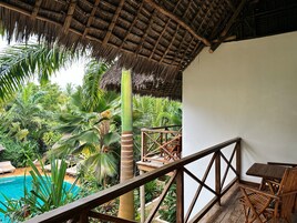Una terraza de madera con techo de paja que da a una piscina y exuberante vegetación tropical.