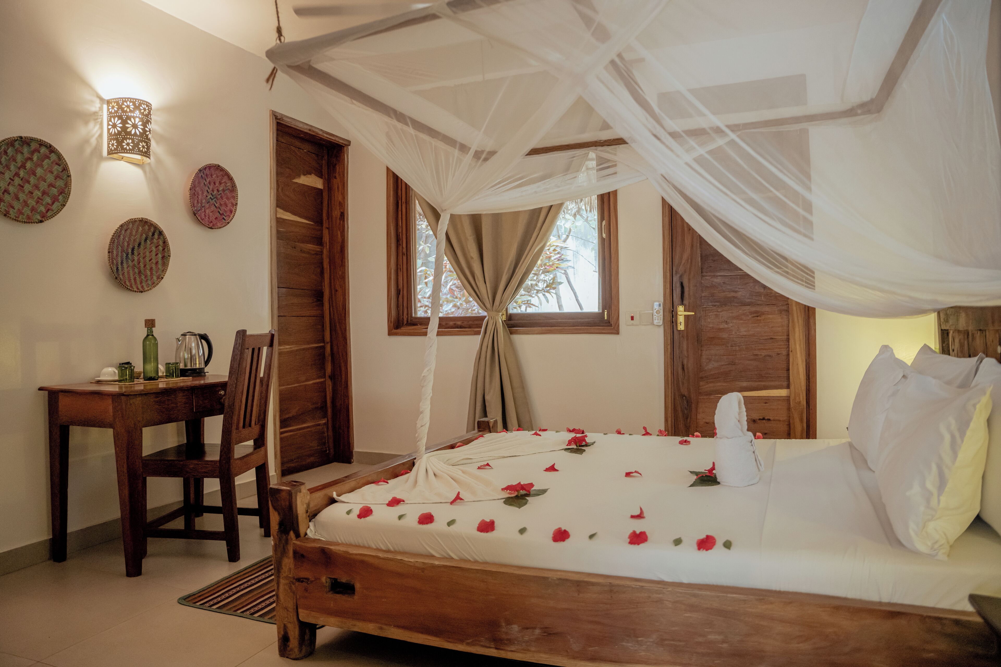 A bedroom with a bed, a wooden desk, a chair, and a window with curtains.