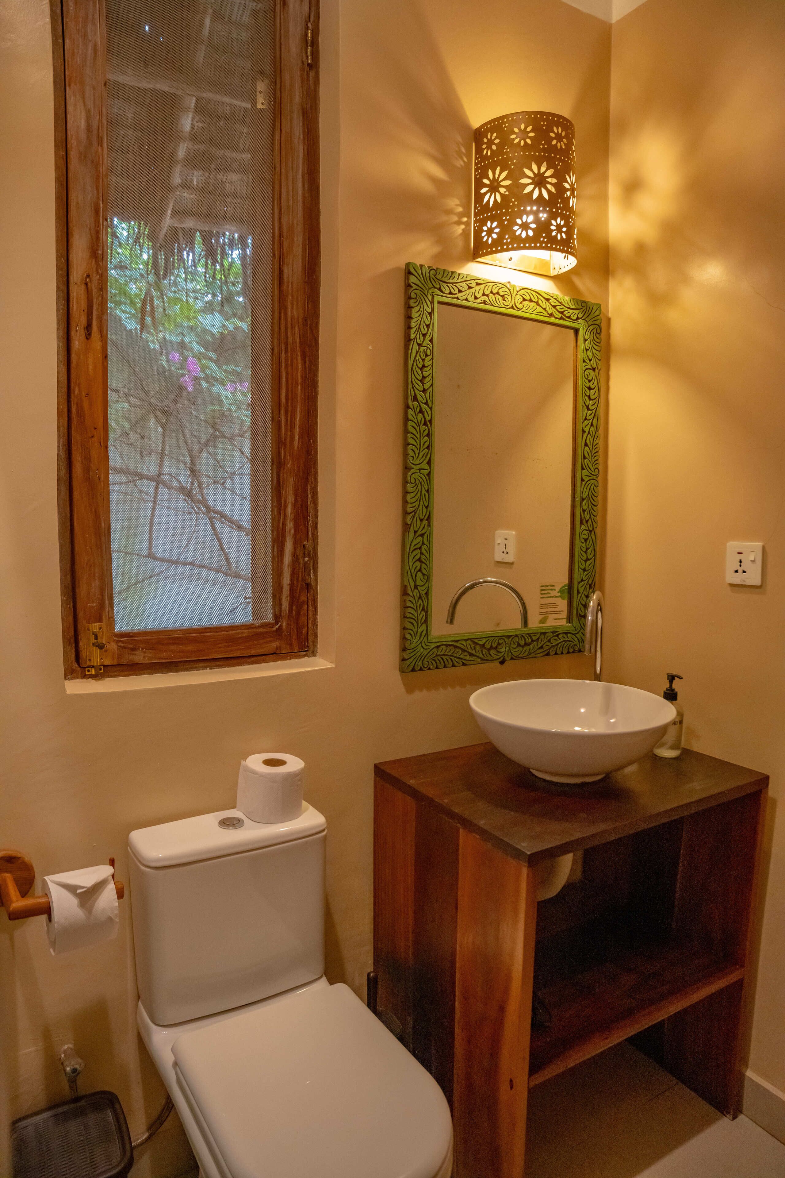 Un baño con tocador de madera, lavamanos blanco y retrete.