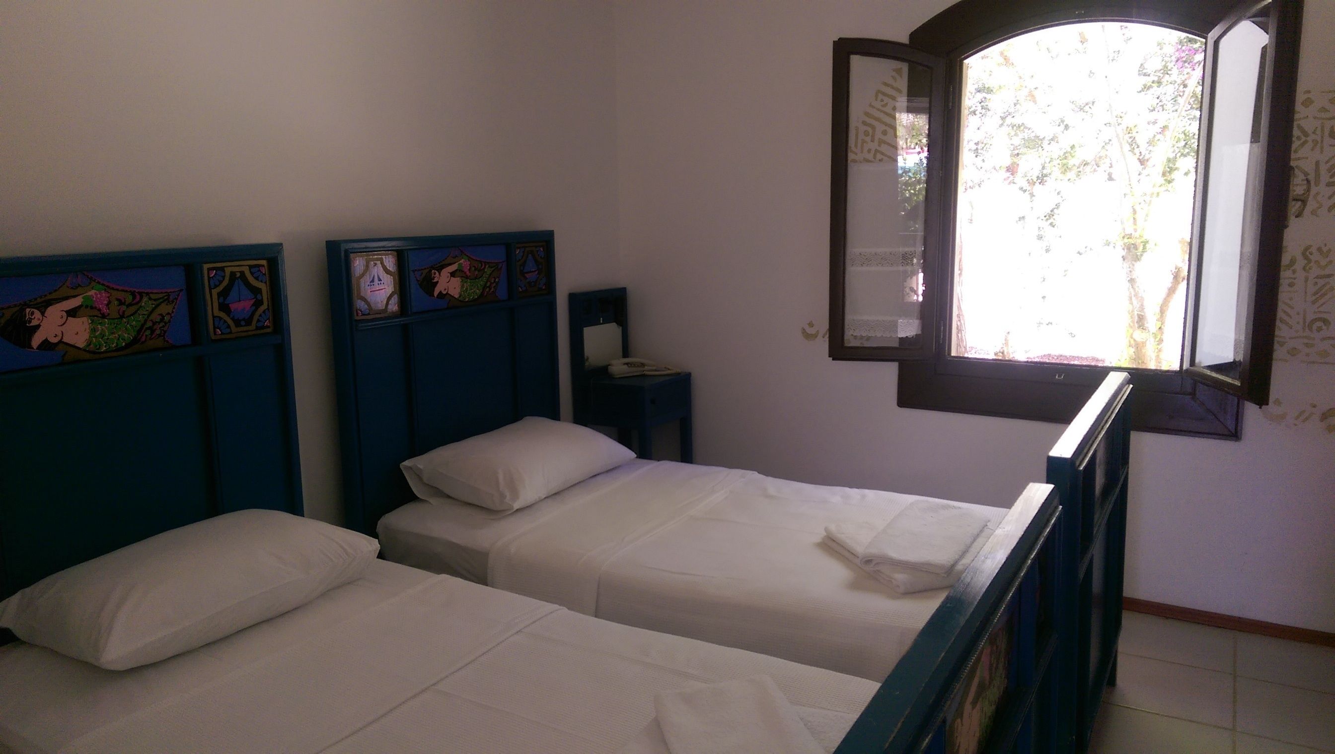 Una habitación con dos camas, una mesita de noche y una ventana con vistas a árboles.