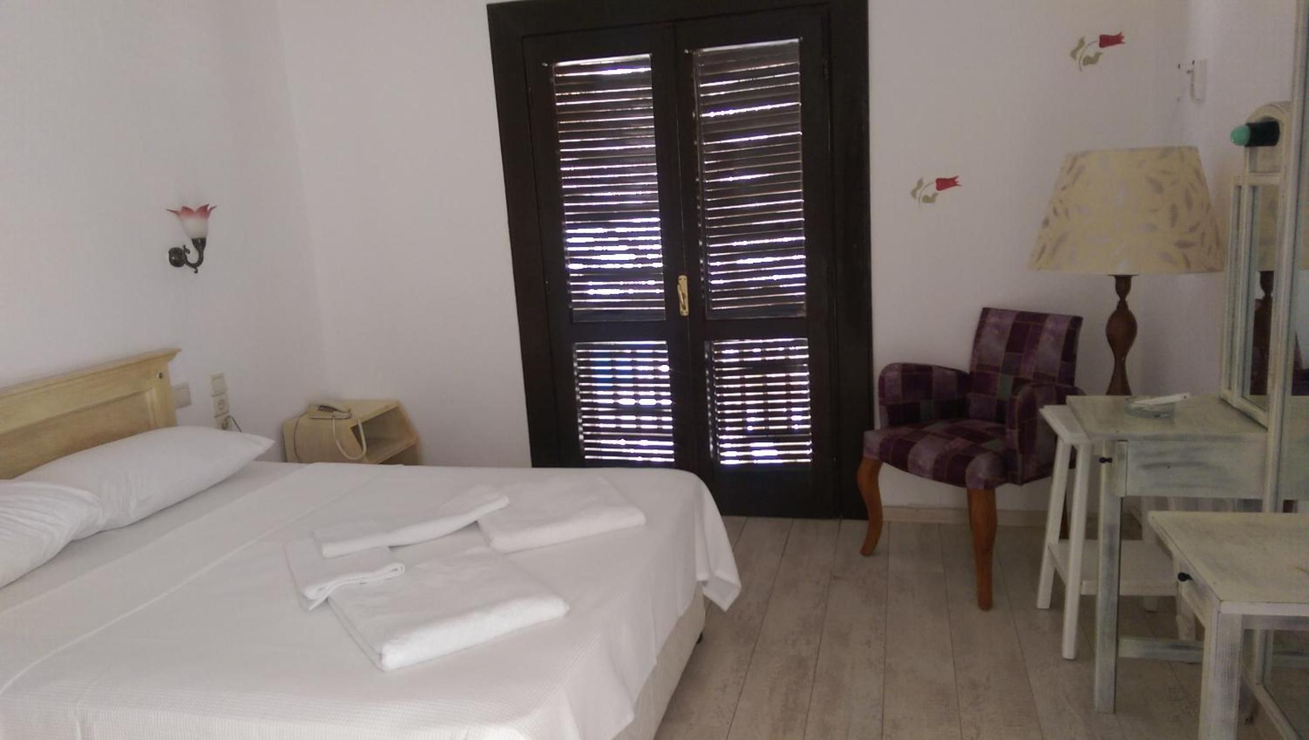 Een hotelkamer met een bed, een stoel, een bureau en een deur voorzien van jaloezieën.