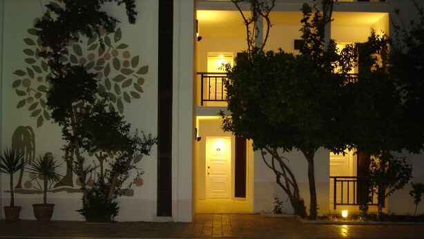 A poolside view of a hotel with a clear pool, potted plants, and a well-lit entrance.