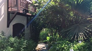 A garden pathway leading to a wooden balcony with a view of lush greenery and a palm tree.