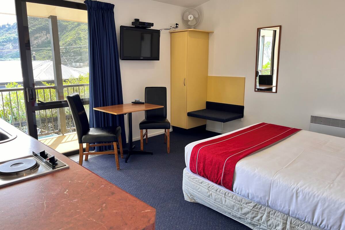 A hotel room with a bed, a desk, a chair, a TV, and a window with curtains.