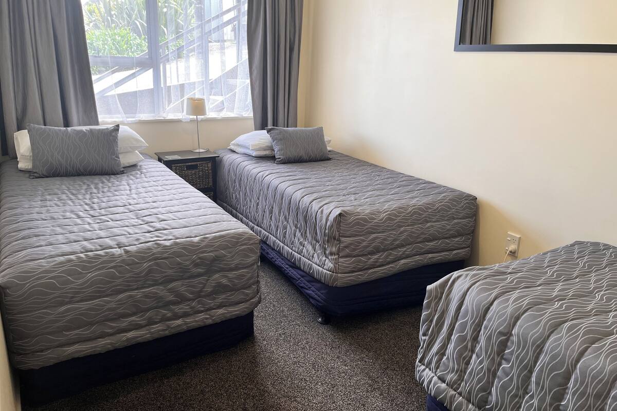 A hotel room with two single beds, a small table, a lamp, and a window with curtains.