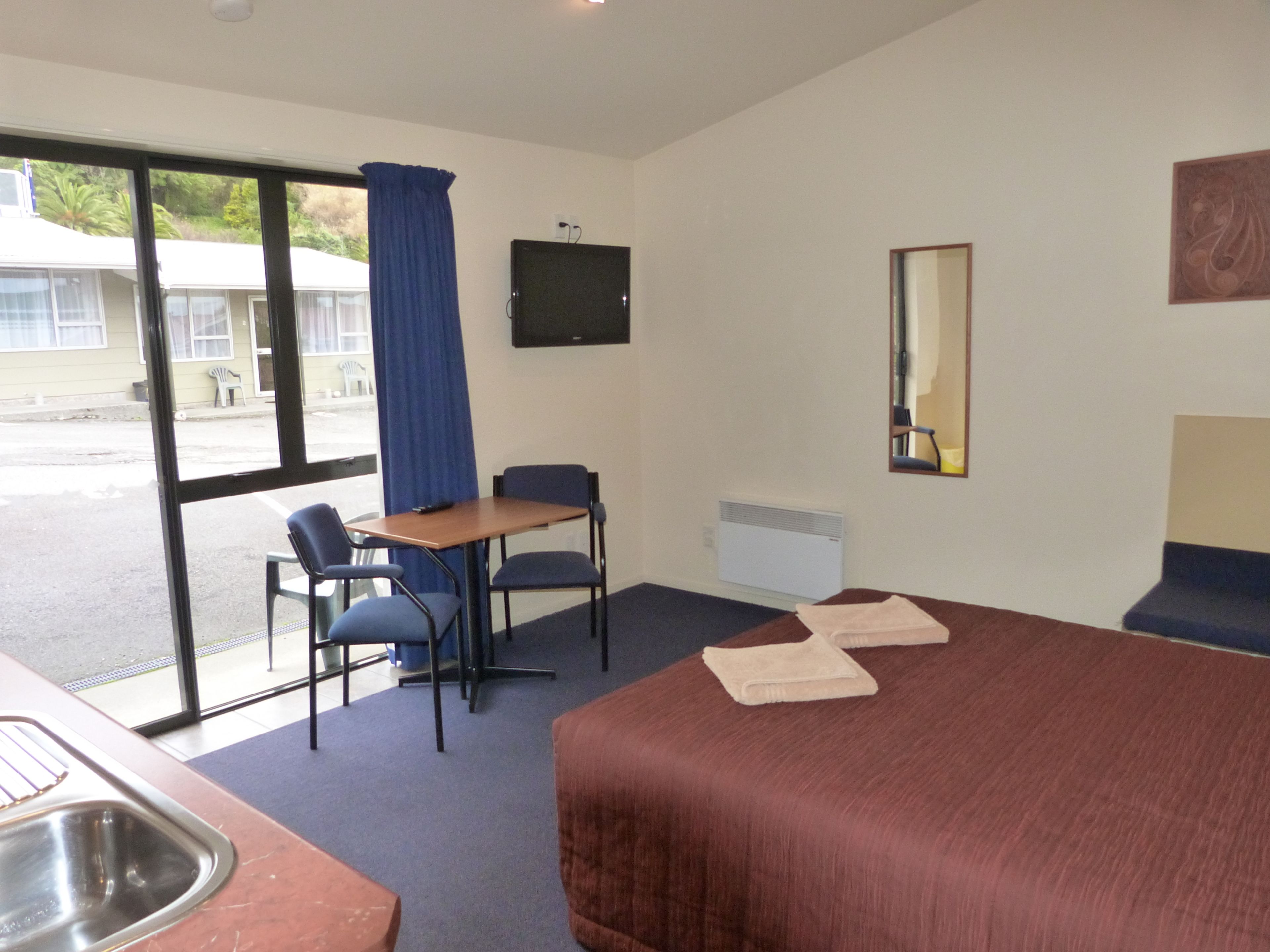 Habitación de hotel con cama, escritorio, dos sillas, televisión, ventana con cortinas, lavabo y espejo.