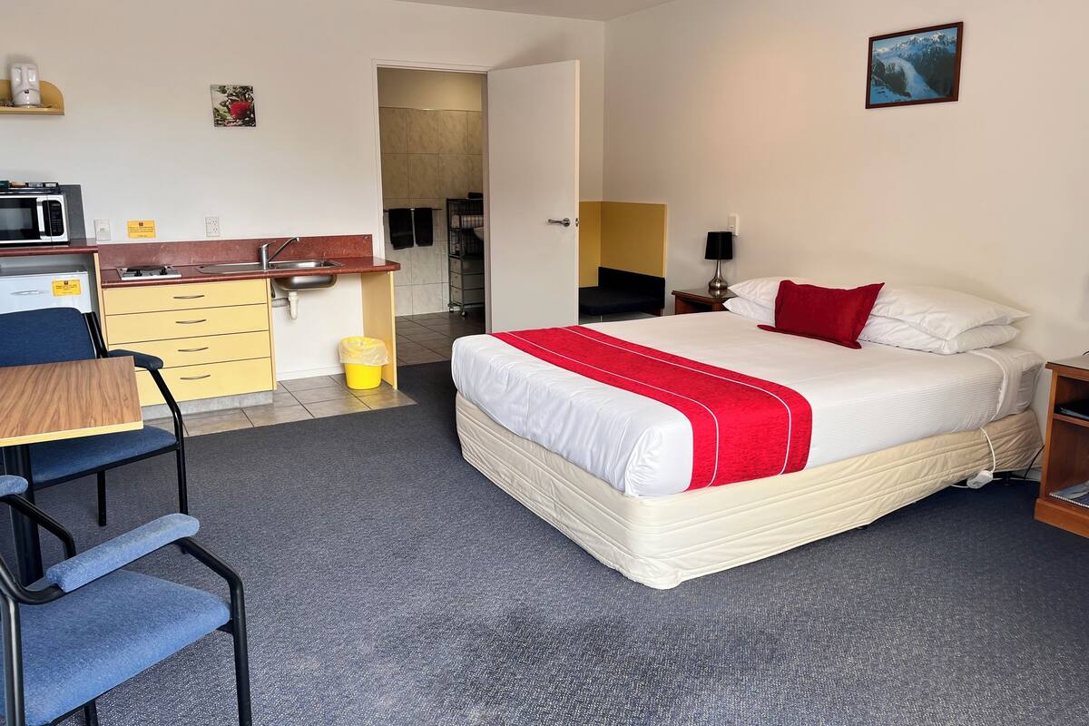 A hotel room with a bed, a desk, a chair, a kitchen area, and a bathroom.