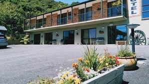 A motel with a two-story structure, a reception desk, and a parking area with a flower bed in the foreground. - Sundowner Motel (Greymouth)