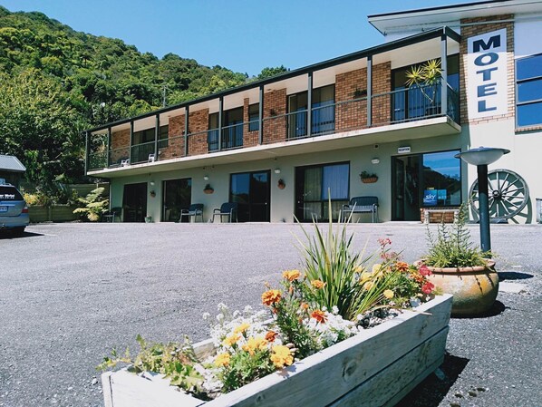 A motel with a two-story structure, a reception desk, and a parking area with a flower bed in the foreground.