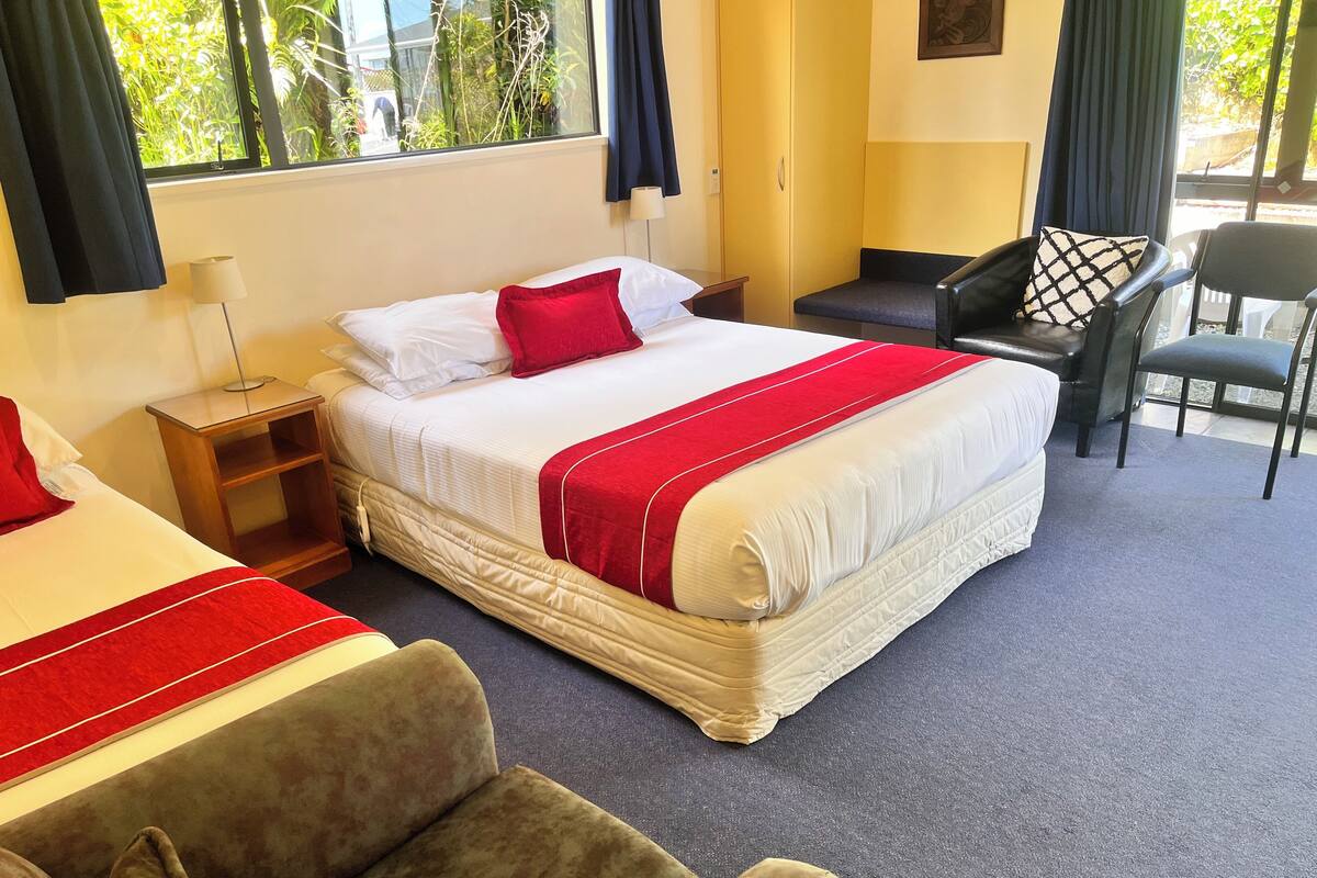 A hotel room with a large bed, two bedside tables, a chair, and a view of greenery outside.