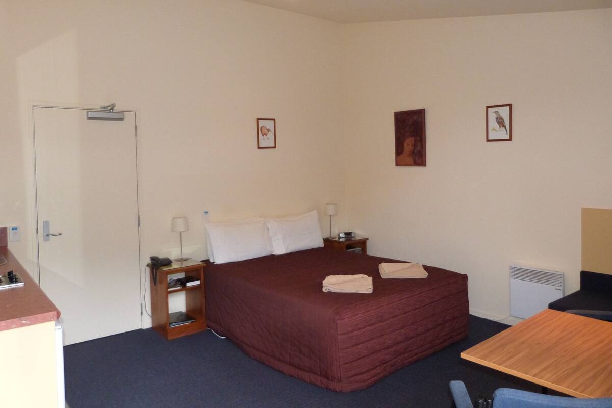 A hotel room with a single bed, bedside tables, a desk, and a chair.