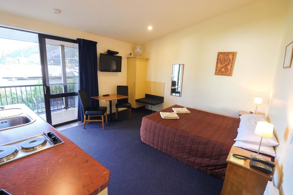 A hotel room with a bed, a desk, a chair, a television, and a balcony.